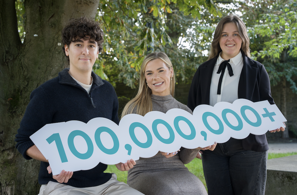 Three people holding a 100 million number sign
